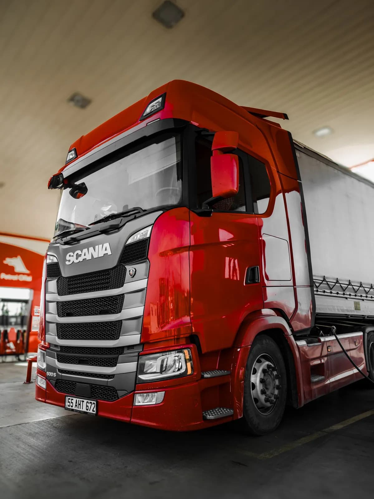 Red truck at a fuel stop mid-route while alpha-TMS sends shipment status updates to customers Red truck at a fuel stop mid-route while alpha-TMS sends shipment status updates to customers